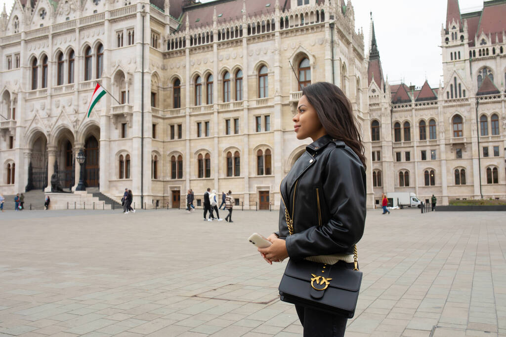 Budapest, Hungría - 22 de octubre de 2022: Feliz joven estudiante disfrutando de una gran vista del edificio del Parlamento en la ciudad de Budapest, viaje en concepto de Europa. - Foto, imagen