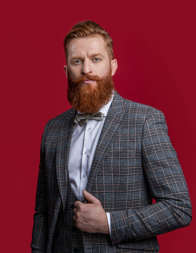 charismatic man in tux bowtie. studio shot of man wearing bowtie and tux. elegant man in formal tux suit with bowtie. tux man with bowtie isolated on burgundy background. - Photo, Image