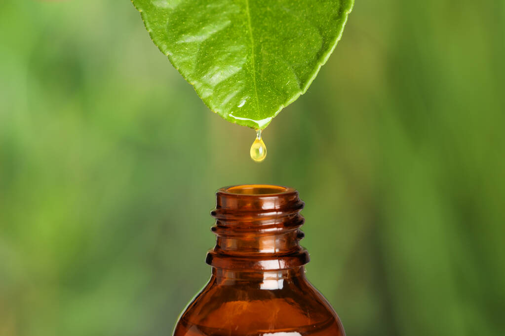 Druppelende etherische olie van blad in fles tegen wazige achtergrond, close-up - Foto, afbeelding