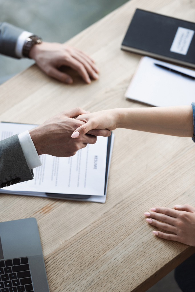 Cropped view of businessman and job seeker shaking hands near blurred resume in office  - Photo, Image