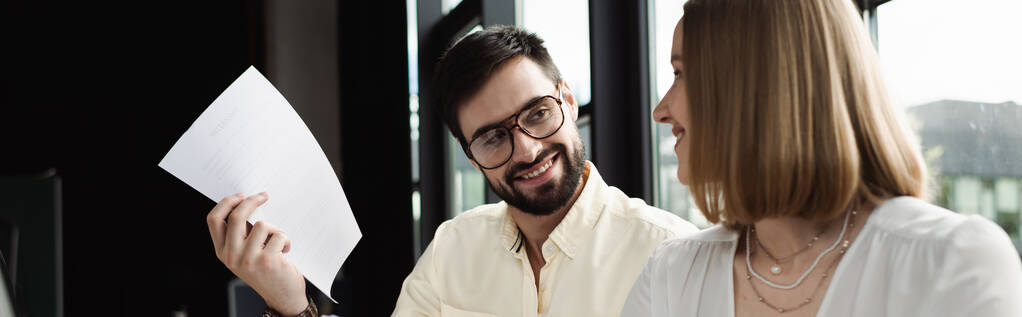 Gestionnaire souriant dans des lunettes tenant du papier près d'un nouveau travailleur au bureau, bannière  - Photo, image