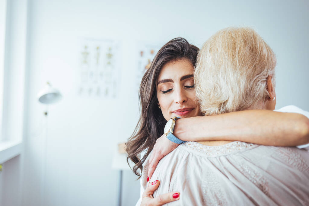 πορτρέτο μιας χαρούμενης γιατρού που αγκαλιάζει τον ηλικιωμένο ασθενή της στην κλινική - Φωτογραφία, εικόνα