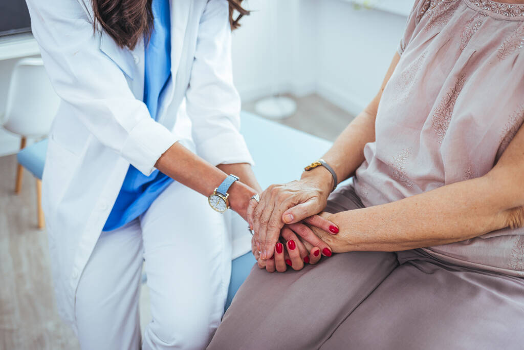 jonge vrouwelijke arts hand in hand van haar senior patiënt in kliniek - Foto, afbeelding