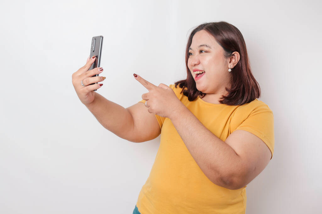 Portrét šťastný asijské velké ženy se usmívá a drží její smartphone na sobě žluté tričko izolované bílým pozadím - Fotografie, Obrázek