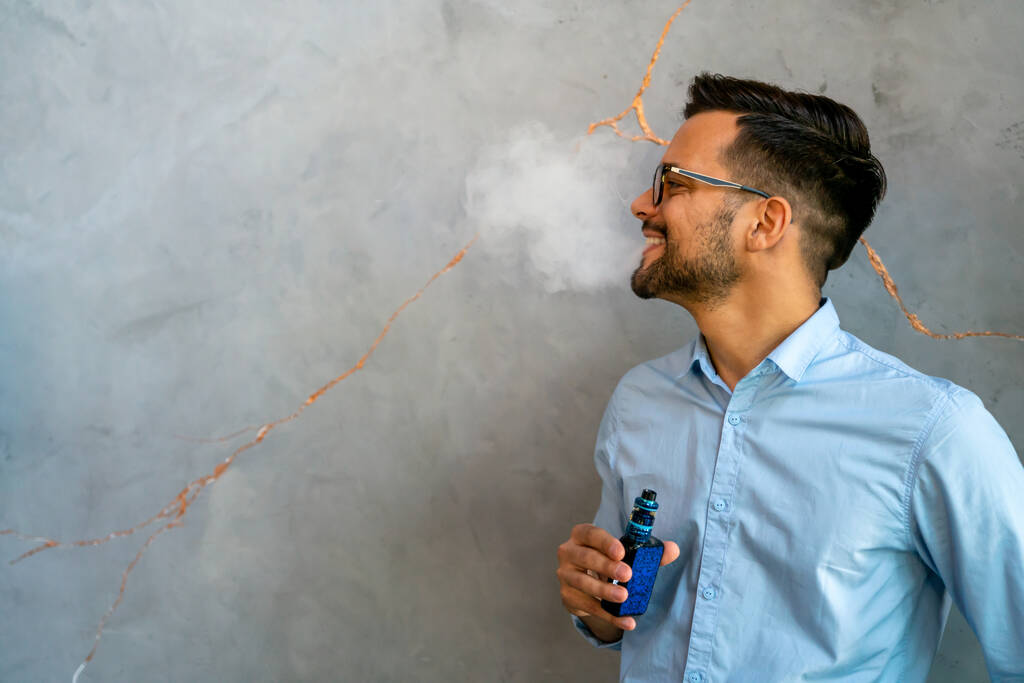 Fumar e vaporizar pode ser pouco saudável e viciante e representar um risco para a saúde dos pulmões. Homem usando e-cigarro. - Foto, Imagem