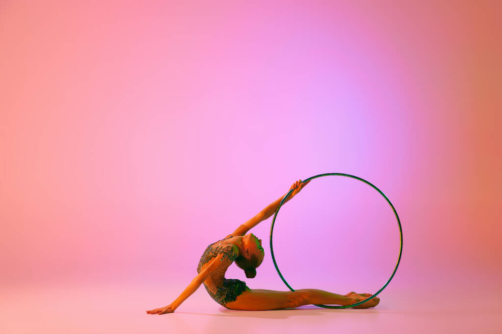 Bella e flessibile atleta aggraziato artista ginnastica ritmica danza, facendo esercizi di stretching isolati su sfondo colorato al neon. Bellezza, arte, sport, competizione, pubblicità e concetto di hobby - Foto, immagini