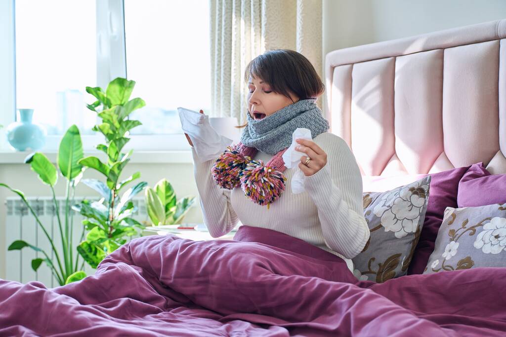 Femme malade tenant un mouchoir, éternuant, essuyant son nez, assise dans son lit à la maison. Problèmes de santé, saison de grippe froide, mode de vie, concept de personnes - Photo, image