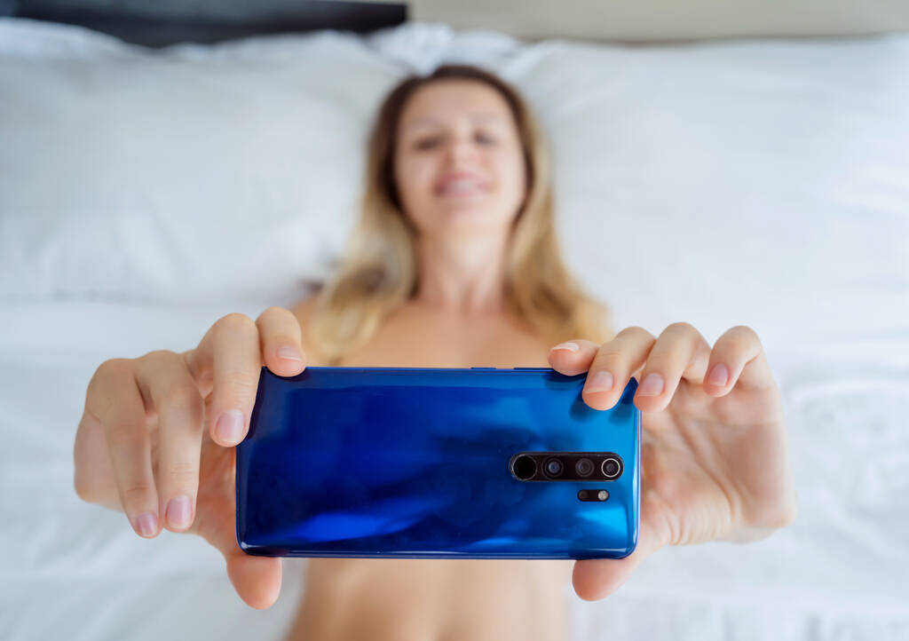 Jeune femme sexy posant devant smartphone dans sa main et travaillant comme modèle webcam. - Photo, image