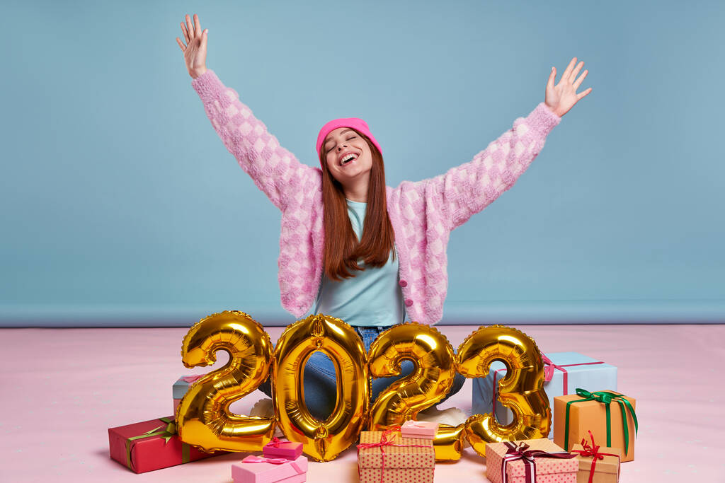 Boldog fiatal nő ül közel az ajándékdobozok és arany színű számok kék háttér - Fotó, kép