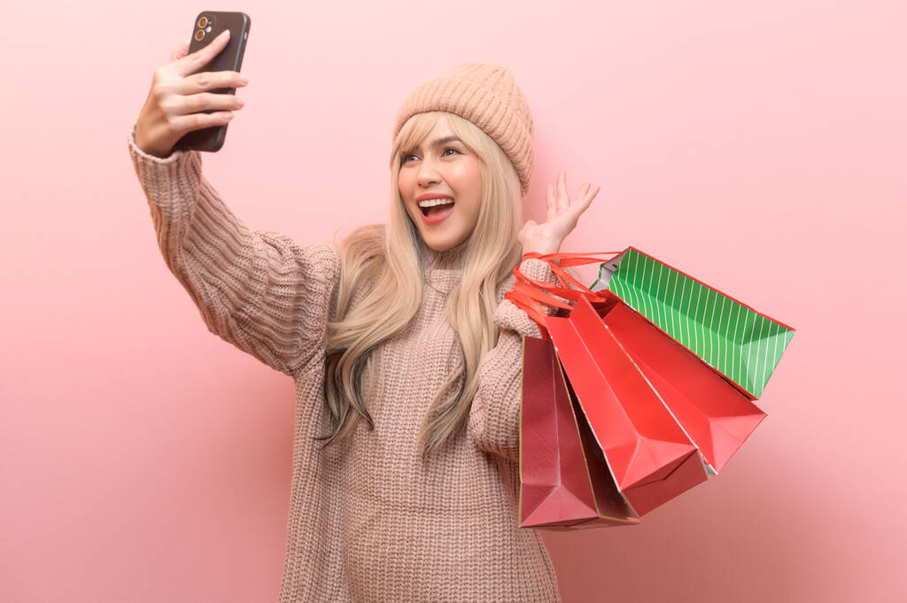 Retrato de mujer joven caucásica con suéter sosteniendo bolsa de compras sobre fondo rosa - Foto, imagen