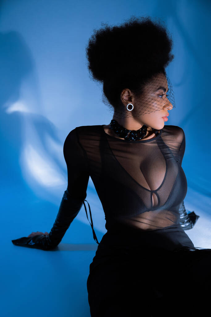 göndör afro-amerikai nő átlátszó ing és fekete fátyol pózol a kék  - Fotó, kép