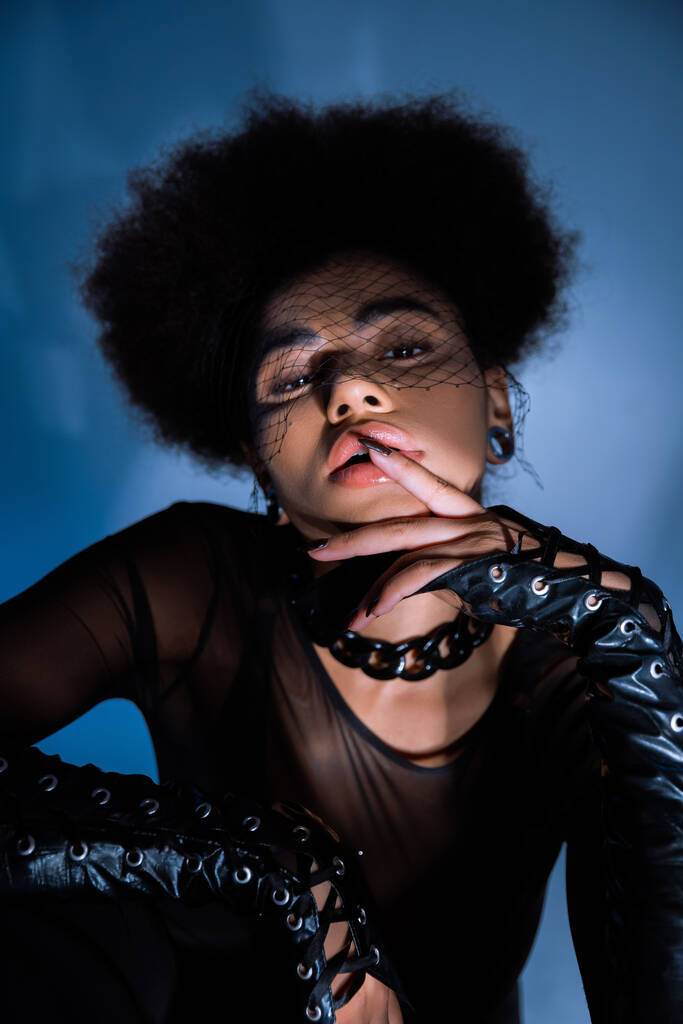 портрет кудрявой африканской американки в черной вуали, смотрящей в камеру, прикасающейся к губе  - Фото, изображение