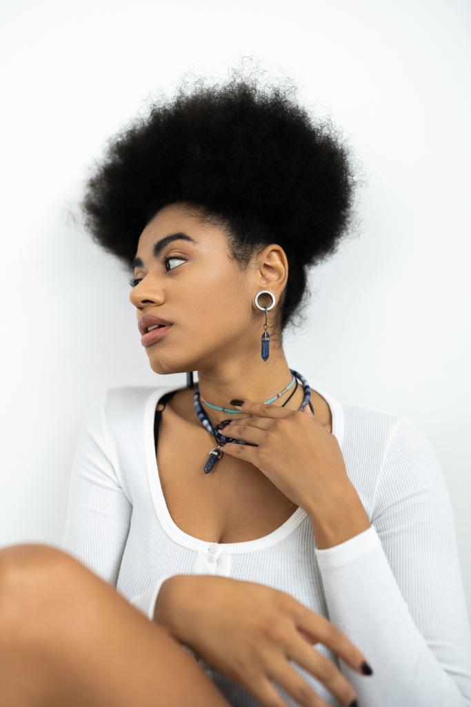 jeune femme afro-américaine aux cheveux bouclés ajustant colliers isolés sur blanc  - Photo, image