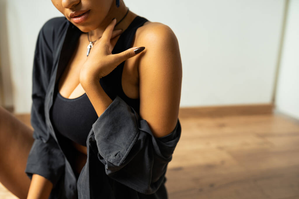 Vista ritagliata della donna afro-americana in crop top e camicia toccando il collo a casa  - Foto, immagini