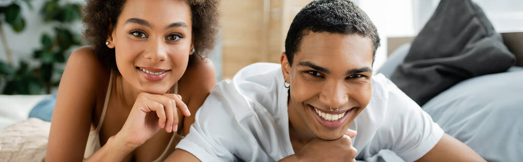 potěšený africký americký pár při pohledu na kameru v ložnici, banner - Fotografie, Obrázek