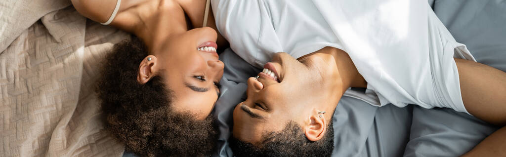 shora pohled na africké americké milence ležící na posteli a usmívající se na sebe, prapor - Fotografie, Obrázek