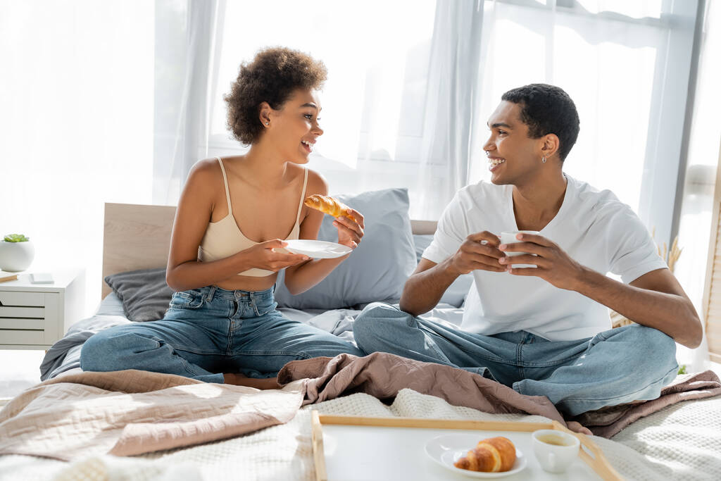 幸せなアフリカ系アメリカ人のカップルがベッドで朝食をしながら - 写真・画像