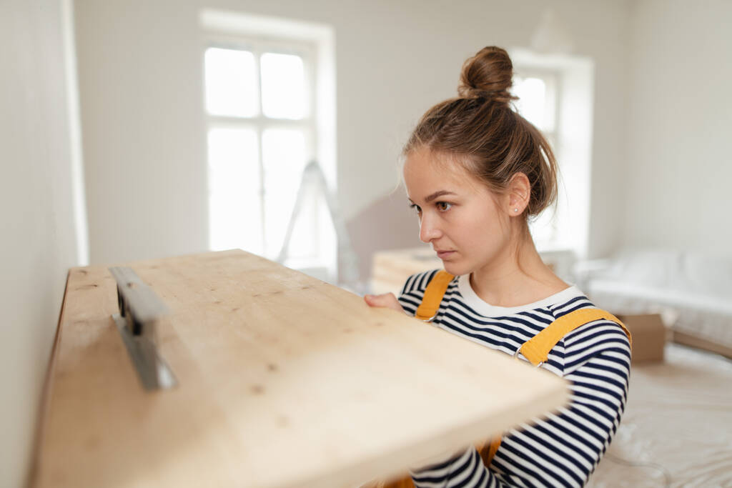 Giovane donna che rifa il suo appartamento, misura il muro con la livella e appende uno scaffale. - Foto, immagini