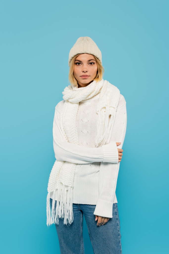young blonde woman in white sweater and winter hat standing isolated on blue - Photo, Image