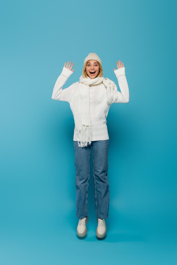 полная длина взволнованной молодой женщины в зимнем наряде и открытого рта левитации на синий  - Фото, изображение
