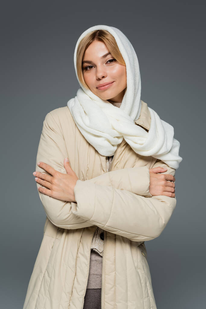 stylish young woman in winter headscarf and puffer jacket standing with crossed arms isolated on grey - Photo, Image