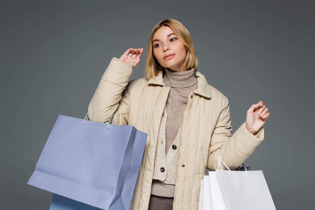 Blonde woman in beige winter outfit holding shopping bags isolated on grey  - Photo, Image