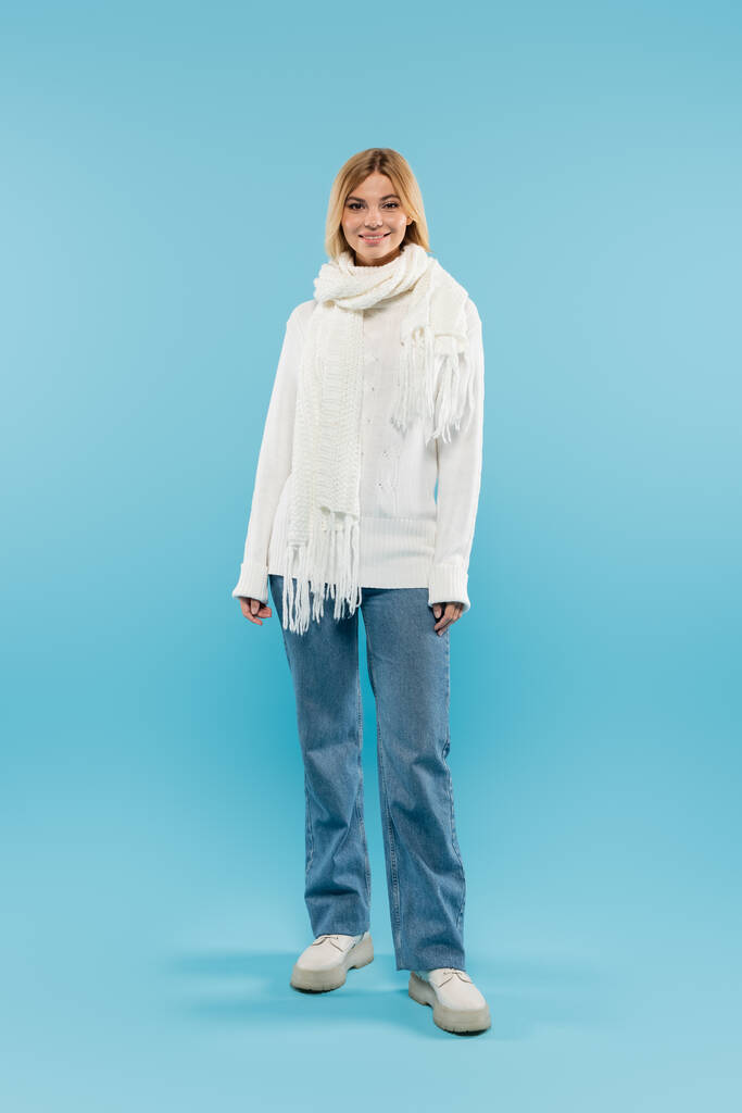 Full length of pretty blonde woman in sweater and jeans looking at camera on blue background  - Photo, Image