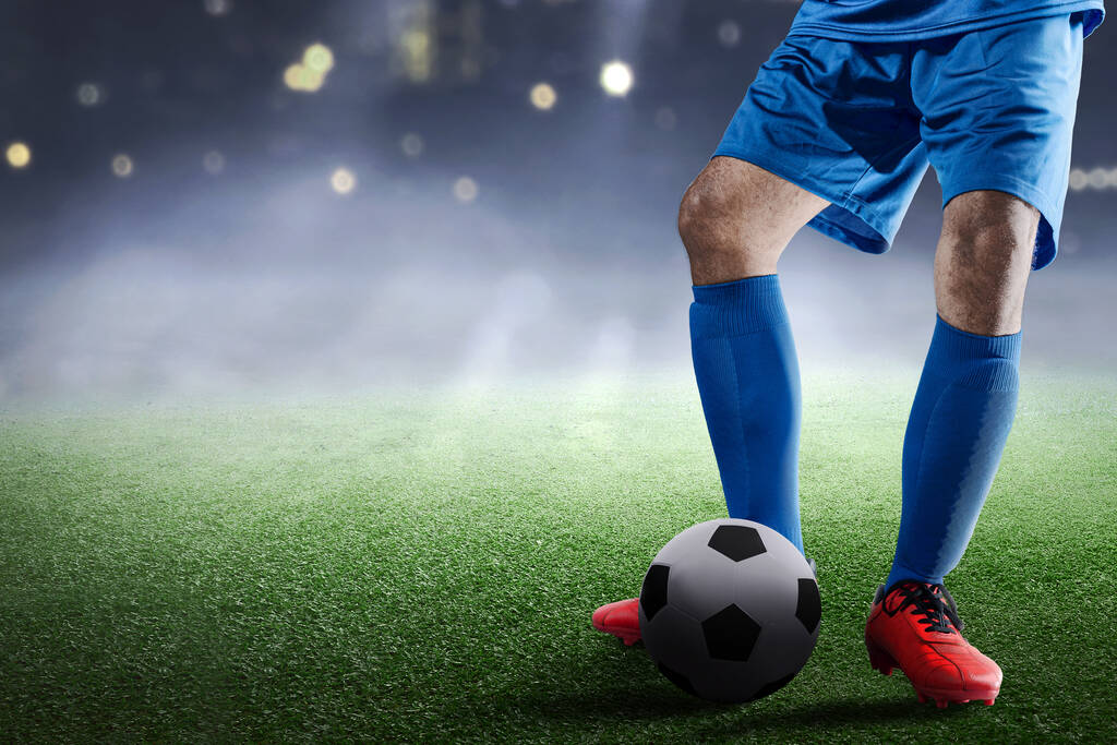 Футболист в синей майке стоит с мячом на футбольном поле - Фото, изображение