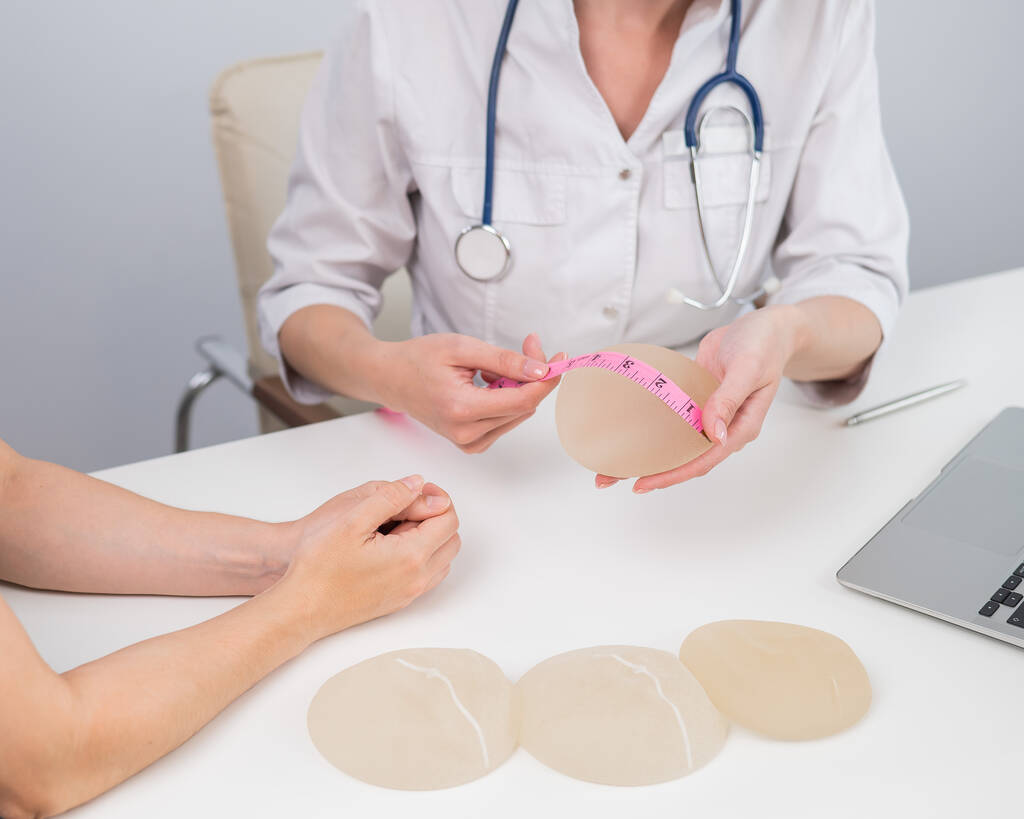 整形外科医は、センチメートルテープで乳房インプラントを測定し、女性患者に示す - 写真・画像