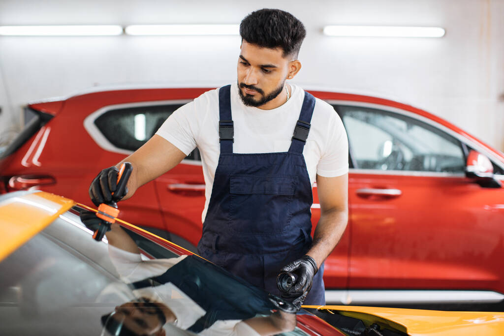 青全体と保護手袋の男性ひげそり労働者は、高級黄色の車のフロントガラスにアンチレインコーティングを適用し、プロの洗車サービスで. - 写真・画像