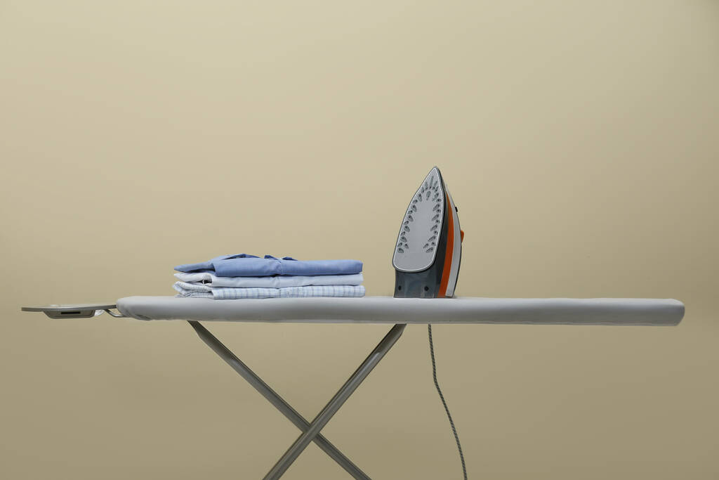 Bej arka plana karşı modern demir ve temiz giysi yığını - Fotoğraf, Görsel