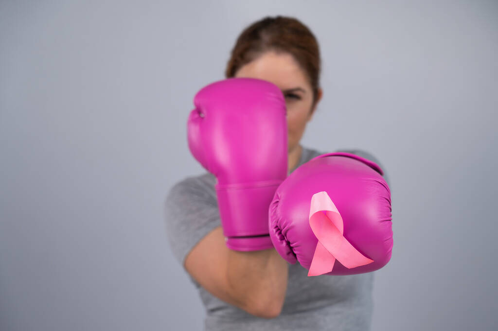 Λευκή γυναίκα με ροζ γάντια πυγμαχίας με ροζ κορδέλα στο στήθος σε γκρι φόντο. Καταπολέμηση του καρκίνου του μαστού - Φωτογραφία, εικόνα