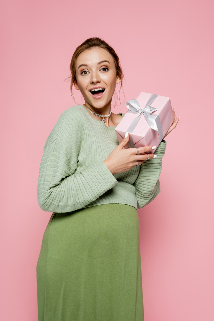 Izgalmas terhes nő zöld ruhában gazdaság ajándék elszigetelt rózsaszín  - Fotó, kép