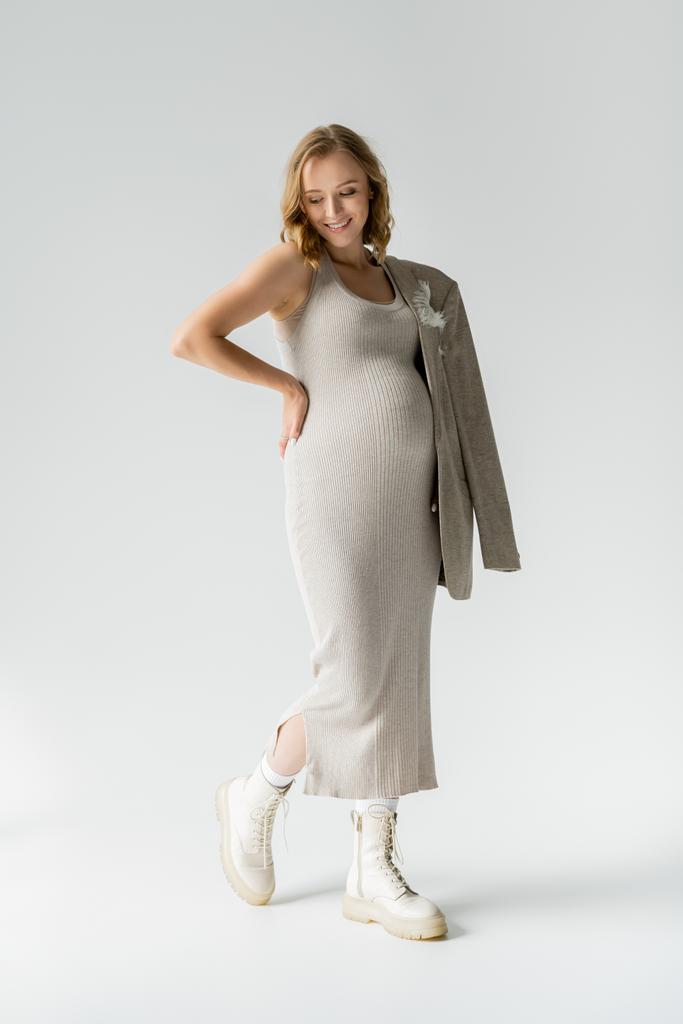 スタイリッシュな妊娠中の女性でドレスとブーツ姿勢上の灰色の背景  - 写真・画像