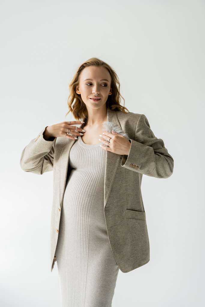 Κομψό έγκυος γυναίκα με φόρεμα και σακάκι κοιτάζοντας μακριά απομονώνονται σε γκρι  - Φωτογραφία, εικόνα