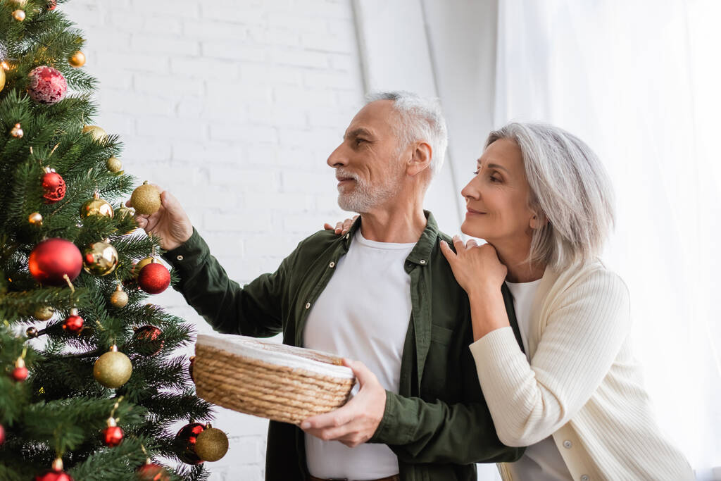 cheerful middle aged woman hugging husband decorating christmas tree - Photo, Image