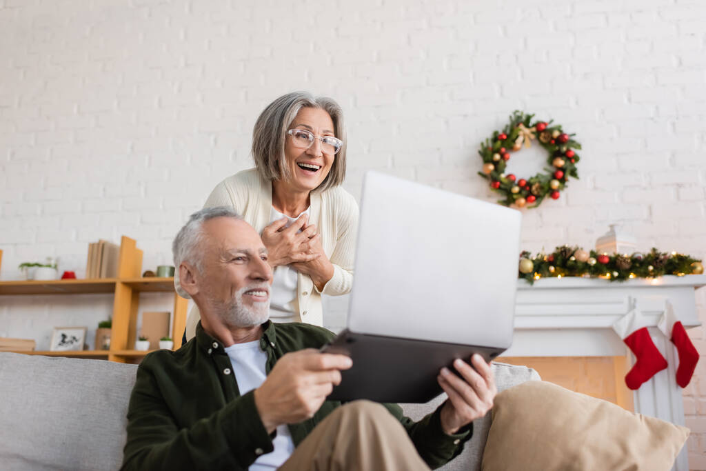 veselý muž středního věku ukazuje notebook polichocen manželka v brýlích na Štědrý den  - Fotografie, Obrázek
