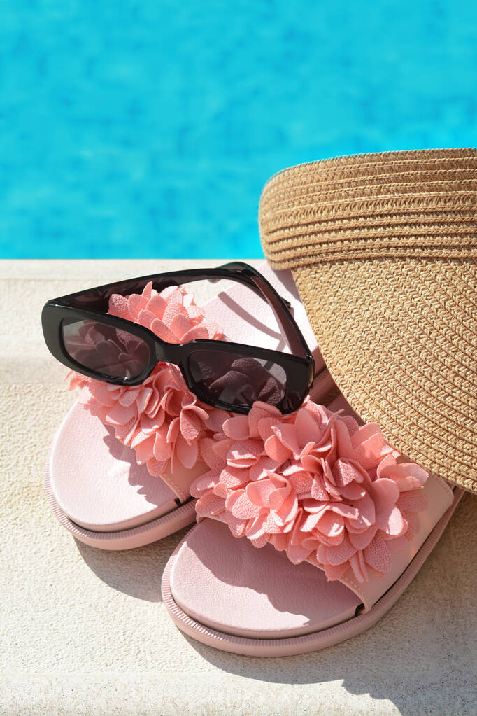 Stylový čapka, pantofle a sluneční brýle v blízkosti venkovního bazénu za slunečného dne, detailní záběr - Fotografie, Obrázek