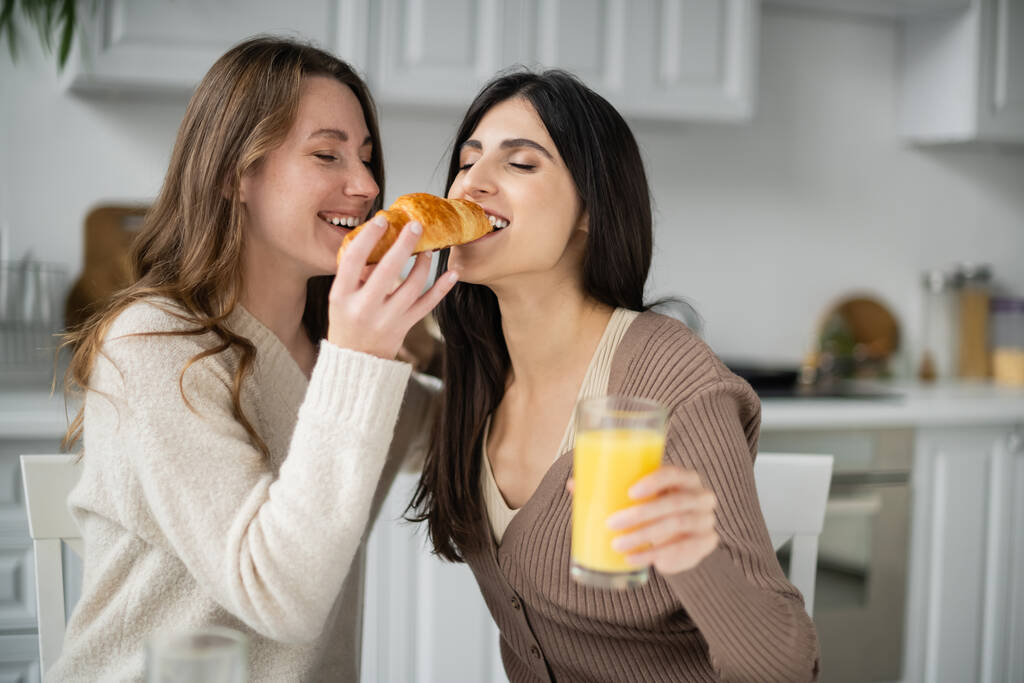 Giovane donna che nutre fidanzata con croissant durante la colazione in cucina  - Foto, immagini