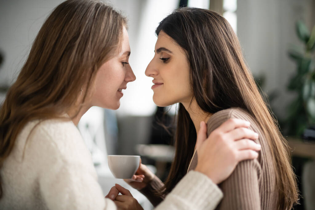 Side view of woman in sweater hugging partner with cup at home  - Photo, Image