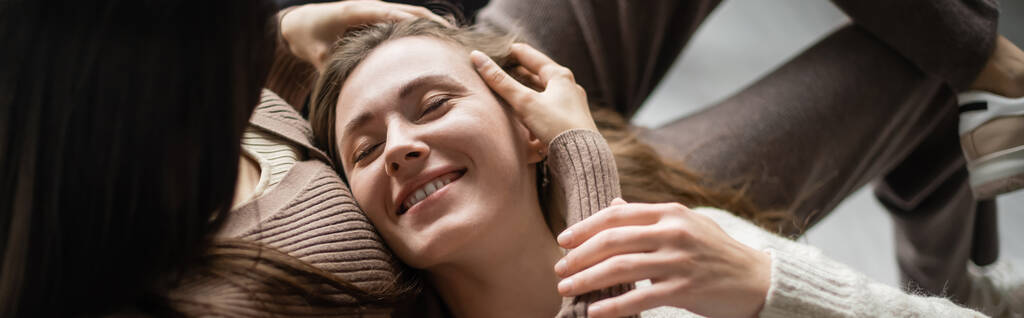 Vue grand angle de la femme touchant partenaire souriant sur le canapé à la maison, bannière  - Photo, image