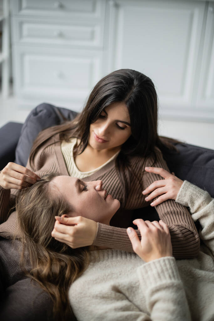 Joven lesbiana tocando novia mientras descansa en el sofá en casa  - Foto, Imagen