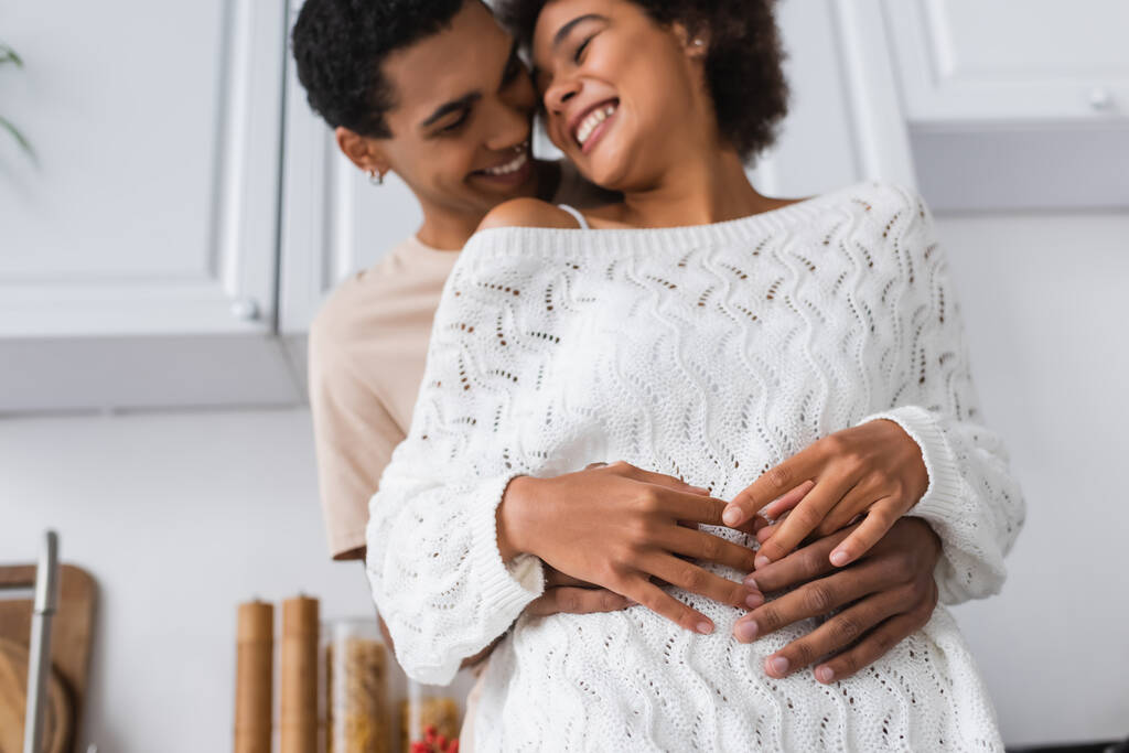 baixo ângulo vista de homem borrado abraçando rindo afro-americana namorada na cozinha - Foto, Imagem