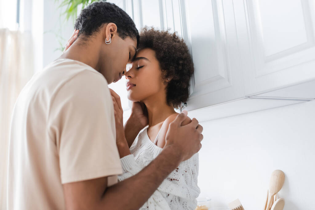 若いアフリカ系アメリカ人のカップルがキッチンで目を閉じて - 写真・画像