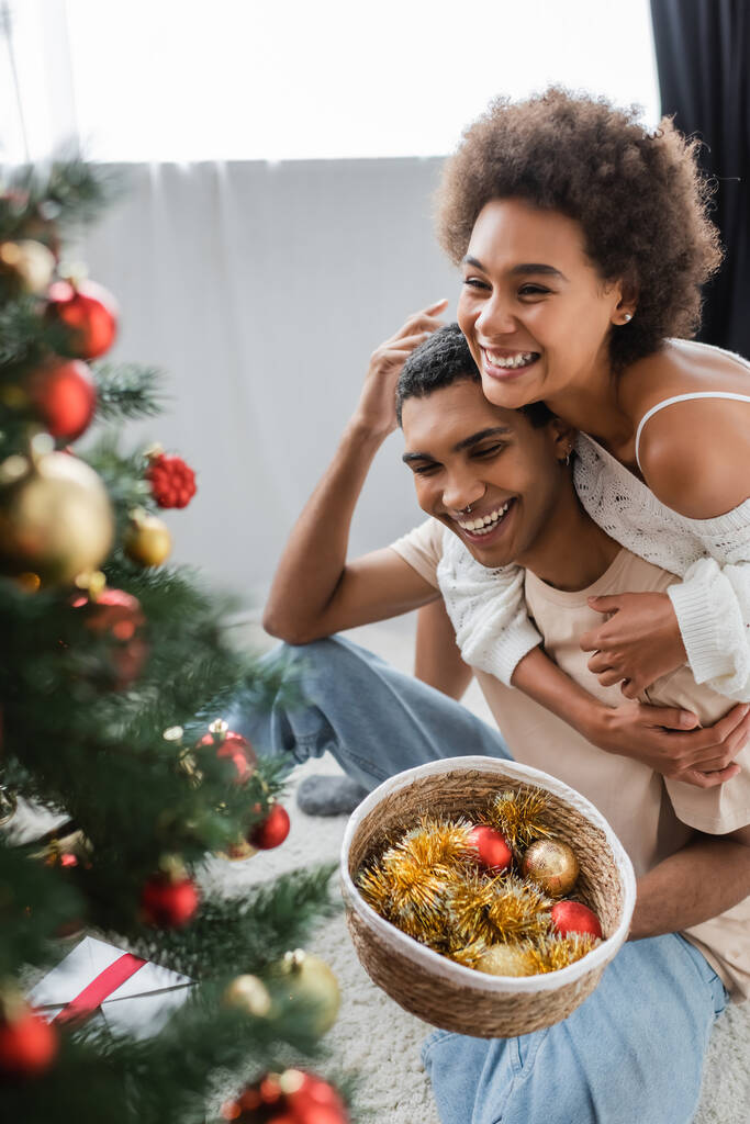 陽気なアフリカ系アメリカ人女性受け入れボーイフレンド保持赤ちゃん近くぼやけたクリスマスツリー - 写真・画像