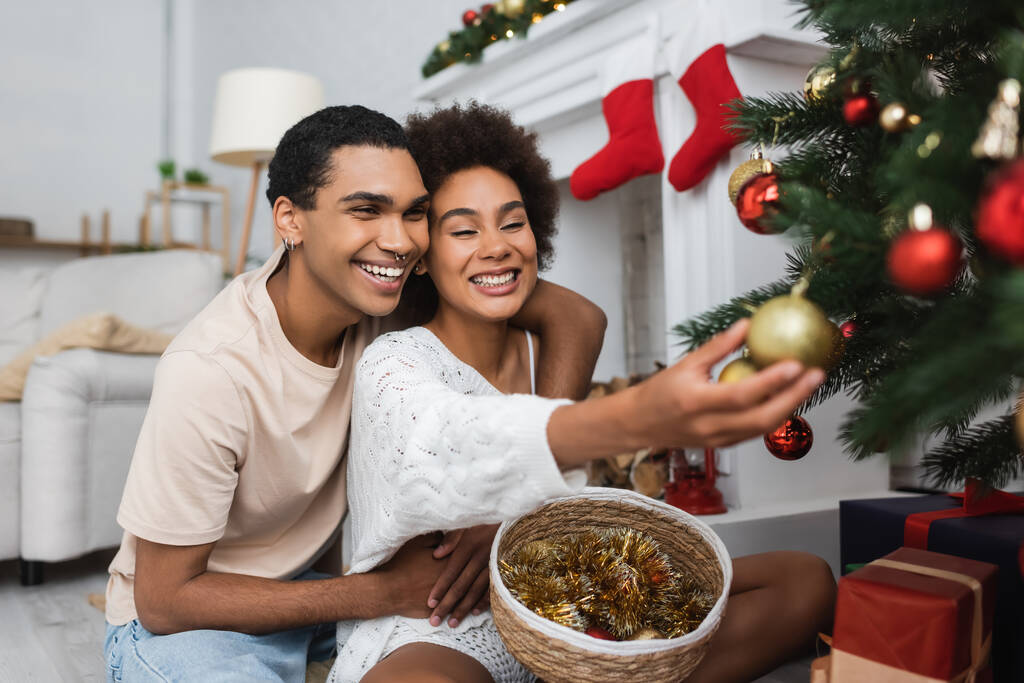onnellinen afrikkalainen amerikkalainen nainen koristelu joulukuusi lähellä poikaystävä ja paju kori tinsel - Valokuva, kuva