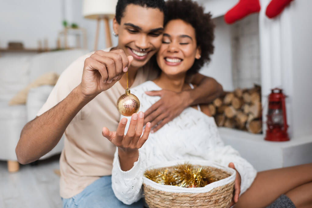 feliz homem americano africano segurando bola de Natal de ouro perto alegre namorada  - Foto, Imagem