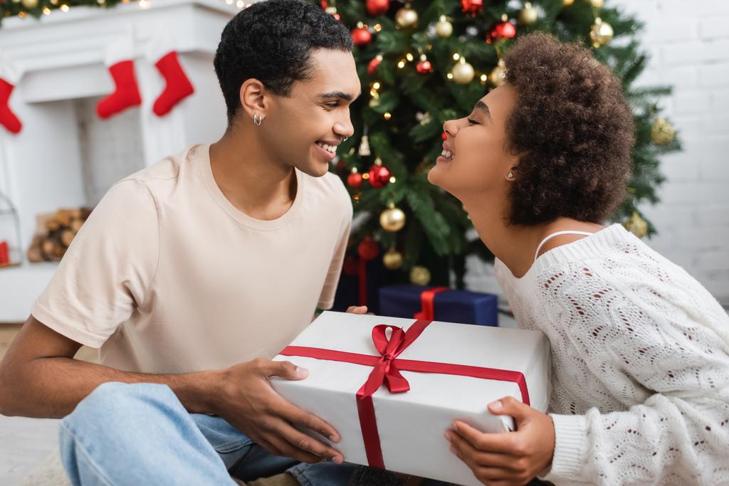 souriant homme afro-américain présentant cadeau de Noël à petite amie heureuse - Photo, image