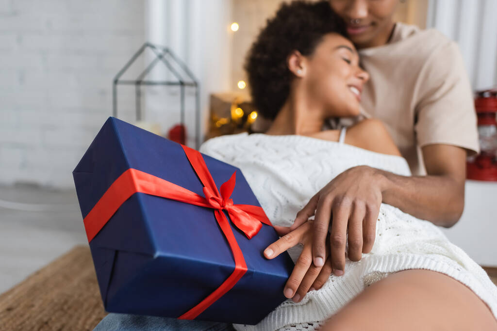 selective focus of blue gift box with red ribbon near blurred african american couple - Photo, Image