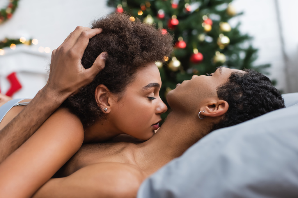 vista lateral do homem americano africano tocando cabelo encaracolado de namorada sexy na cama - Foto, Imagem